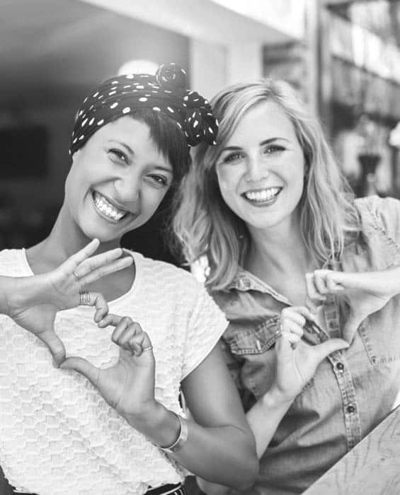 two woman holding up heart symbol with hands smiling